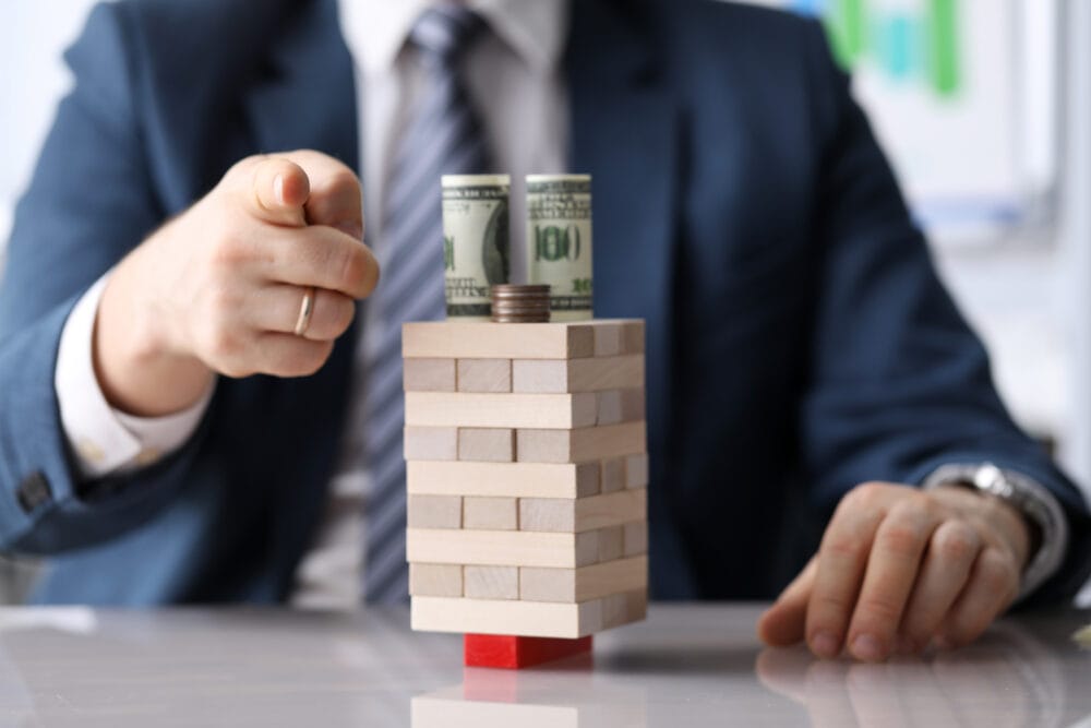 do debt consolidation programs work - man pointing at the camera over Jenga puzzle with money balanced on top