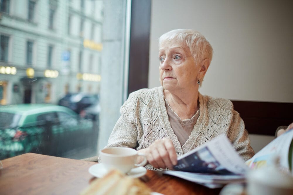 social security widow benefits - Tense woman with journal looking through window while sitting in cafe